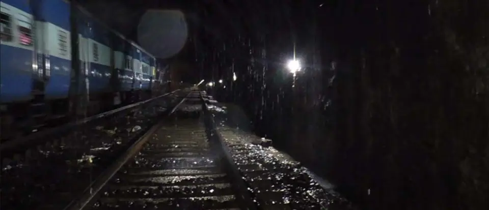 A passenger train passing through the Parsik tunnel while water runs onto the track