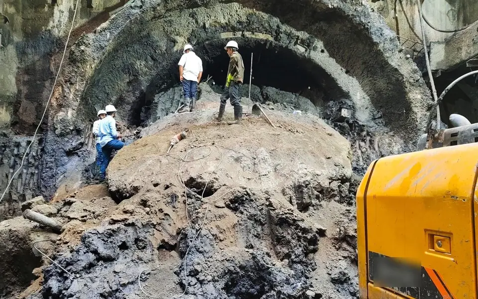 Work in progress in tunnel T-12, Manipur: an arched excavation in soil, with four people in hard hats on the muck and an excavator at the right