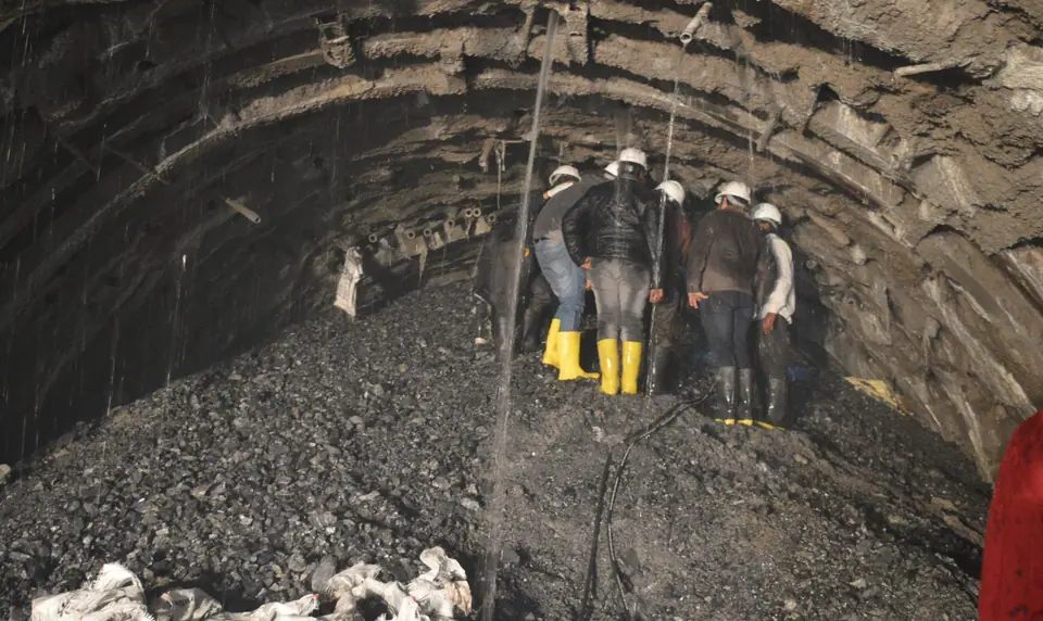 Engineers in hard hats and boots at the face of USBRL tunnel T-5, with water falling from the crown