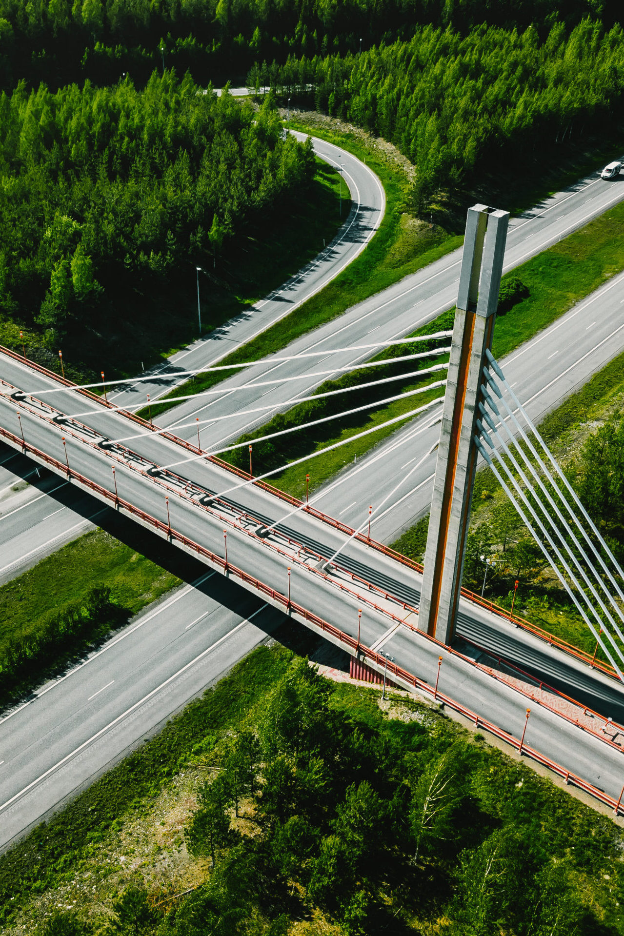 Aerial top view of cable-stayed Suspension bridge and Highway road with green forests on a summer day in Finland.