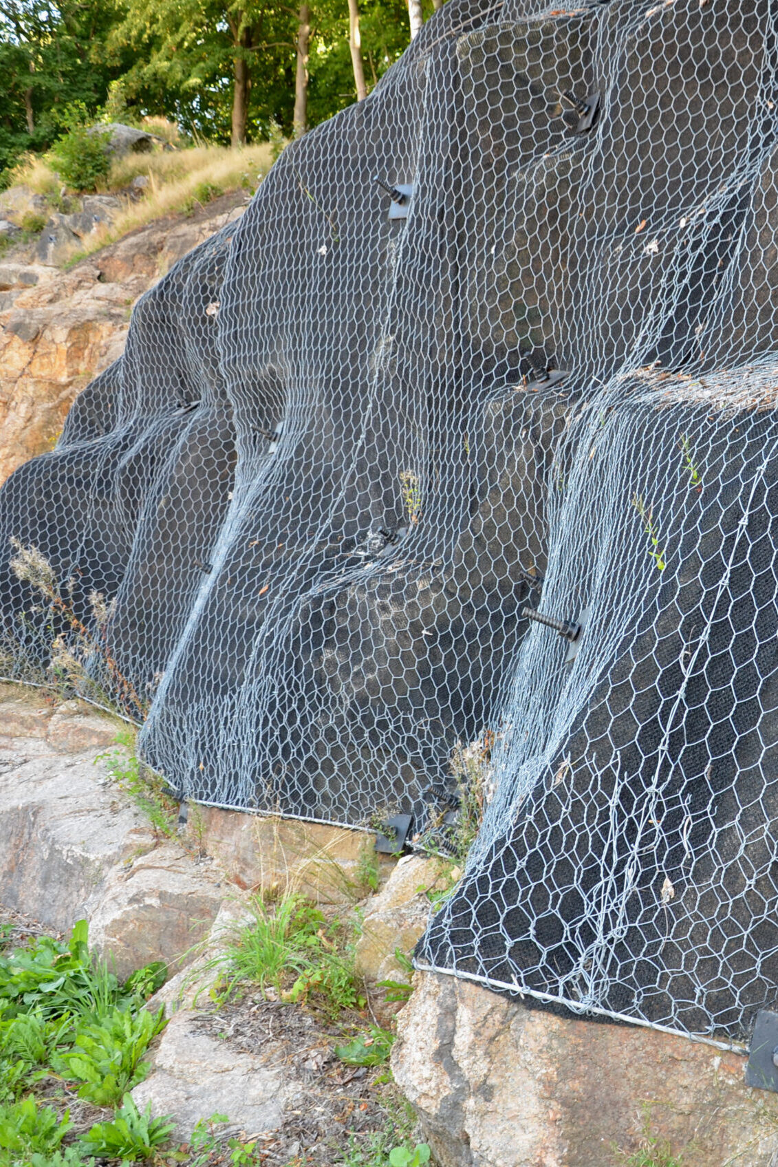 reinforcing slope with steel net anchored deep into rock. falling loose rock stones do not fall on road. anchored with steel nails with nuts. drilled into subsoil and fasten the mesh, train track